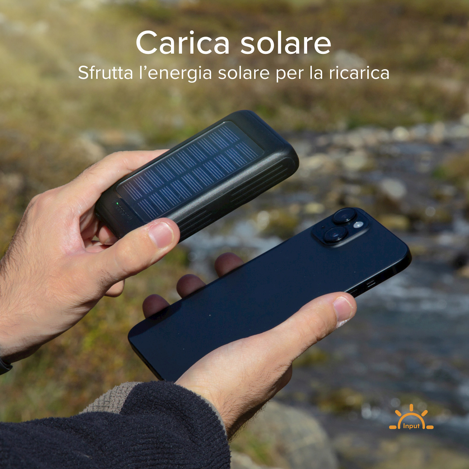 Una persona tiene in mano un power bank solare nero e uno smartphone davanti a uno sfondo naturale.