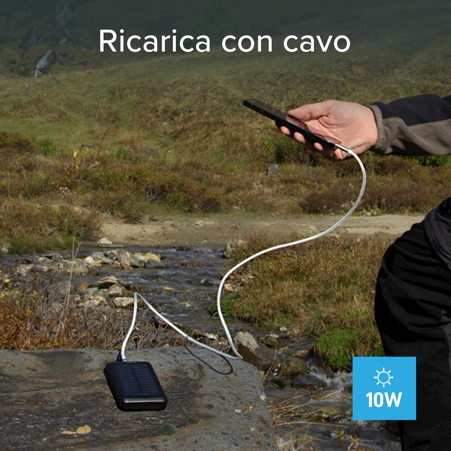 Uno smartphone viene ricaricato all'aperto con un cavo da un power bank solare su una roccia.