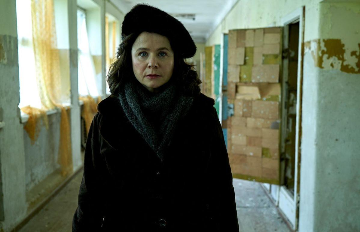 Eine Frau mit Pelzmütze und Schal steht in einem heruntergekommenen Flur.