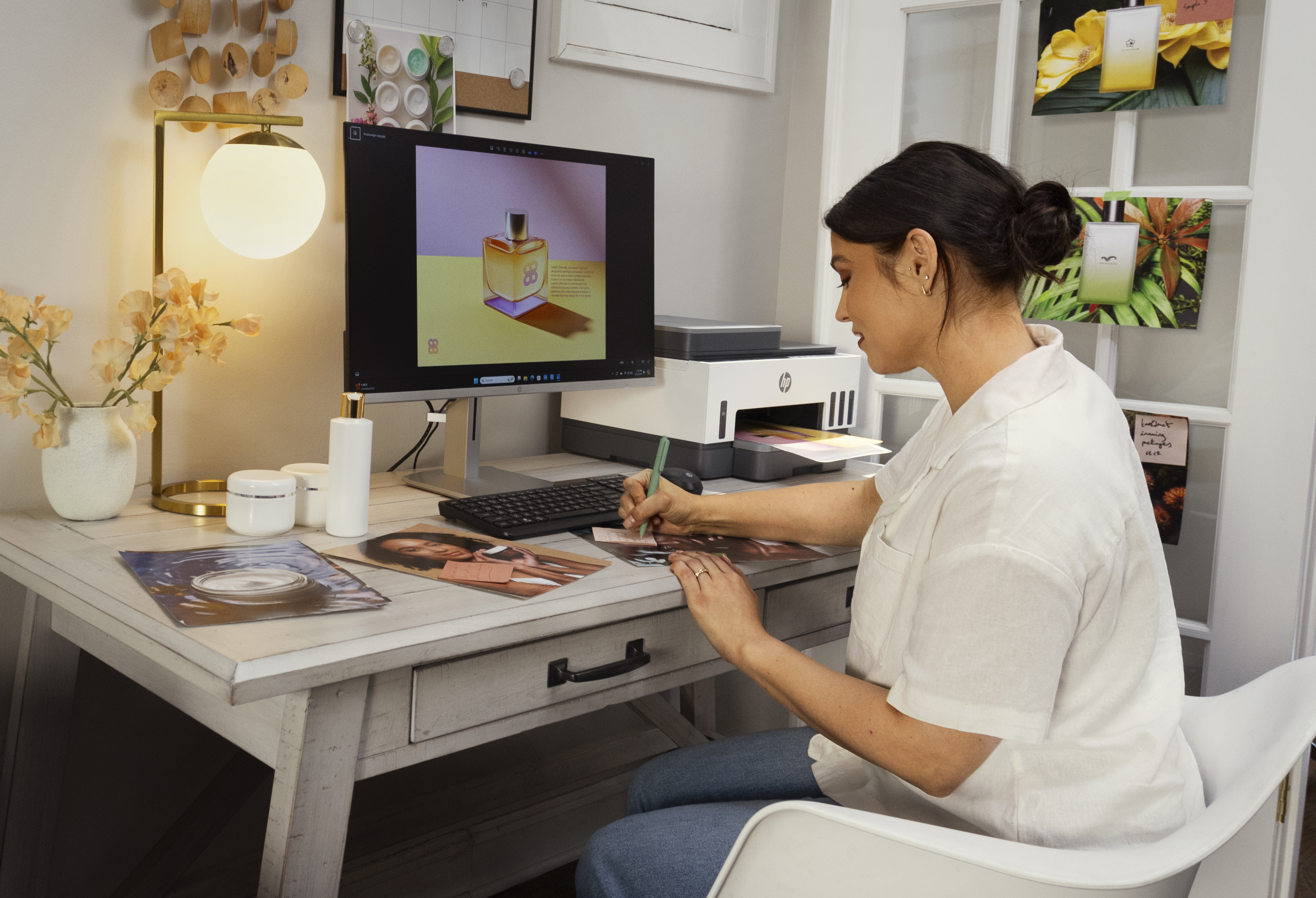 Eine Frau arbeitet an einem Schreibtisch mit Computer, Drucker und Lampe.