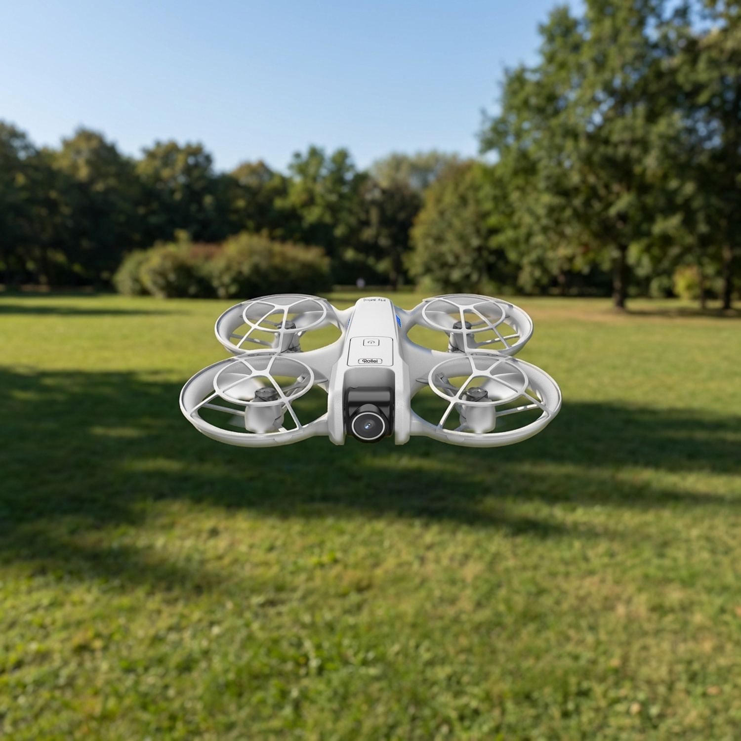 Un piccolo drone bianco con protezioni per eliche vola su uno sfondo di erba verde e alberi.
