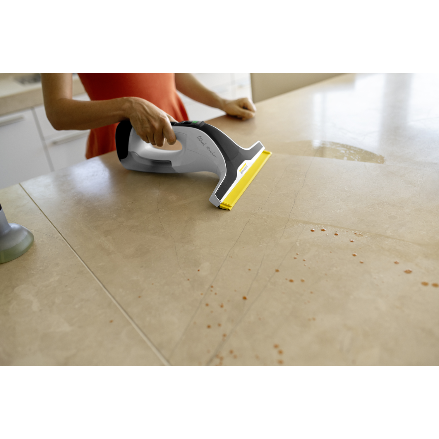 Iemand gebruikt een grijze ruitenreiniger met gele wisser om een beige aanrechtblad schoon te maken.
