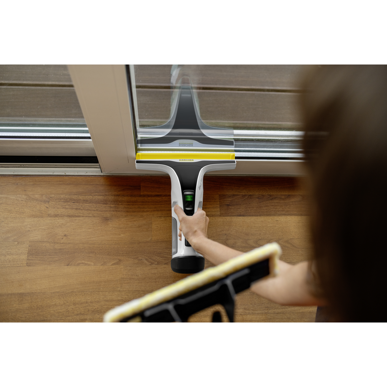 Een persoon gebruikt een Kärcher raamzuiger om een glazen deur op een houten vloer te reinigen.