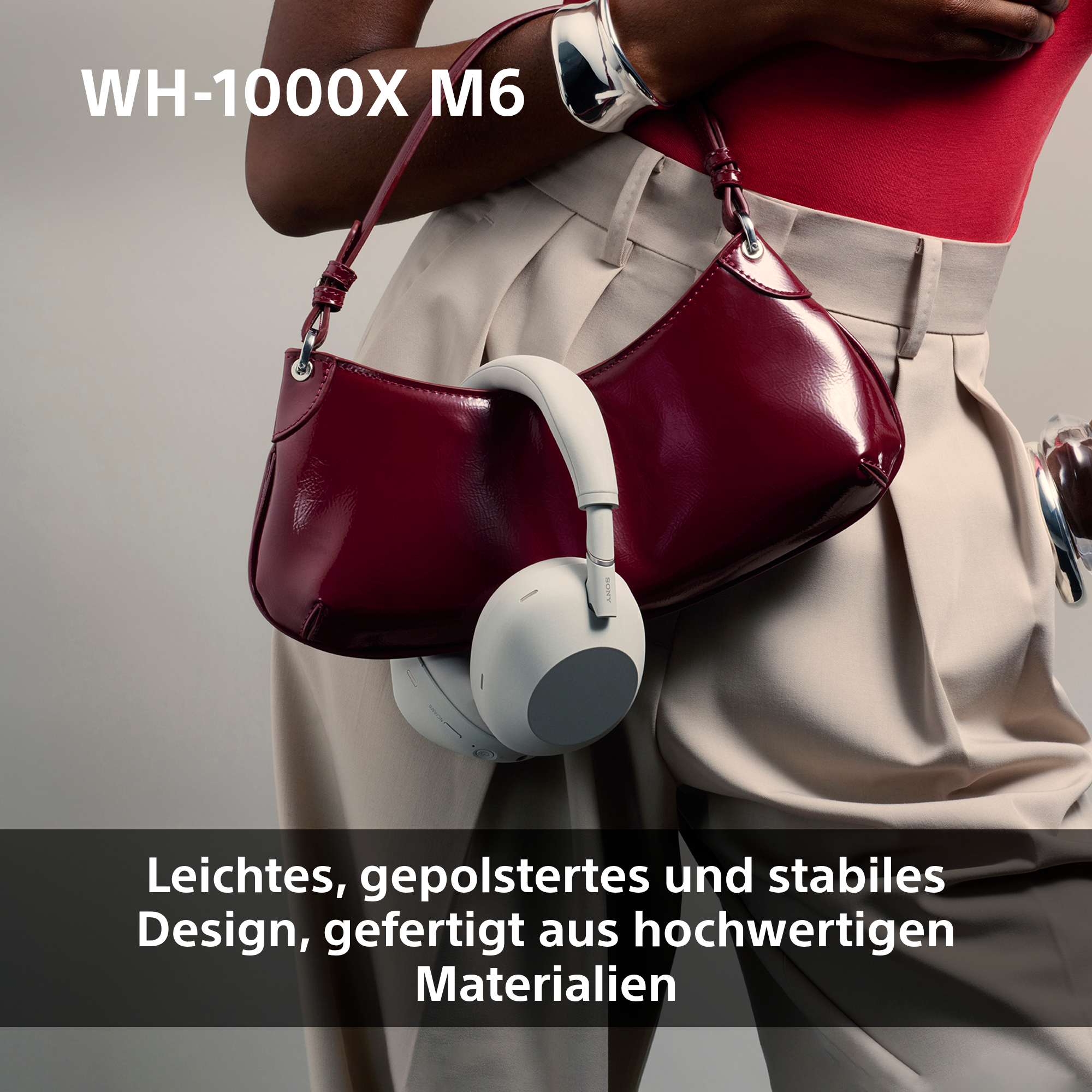 Weiße Kopfhörer hängen an einer dunkelroten Handtasche, getragen von einer Person in heller Hose und rotem Oberteil.