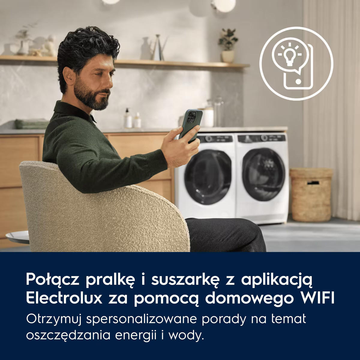 Mężczyzna siedzi w fotelu i korzysta ze smartfona w kuchni z pralką i suszarką.