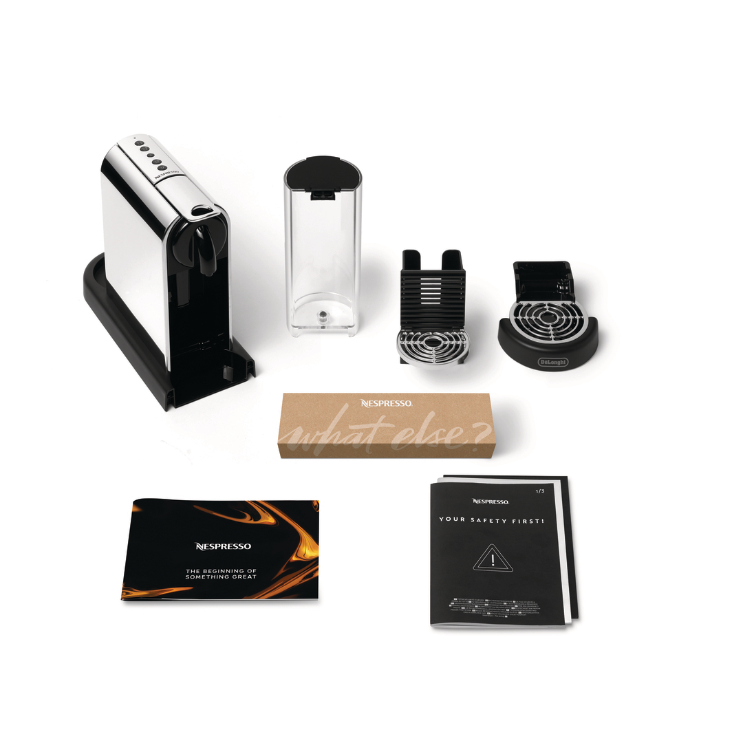Eine chromfarbene Nespresso-Kaffeemaschine mit abnehmbarem Wassertank, Zubehör, einer Box und Handbüchern auf weißem Hintergrund.