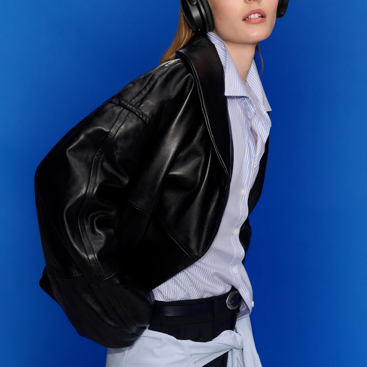 Une personne portant une veste en cuir noir, une chemise à rayures bleues et un casque sur fond bleu.