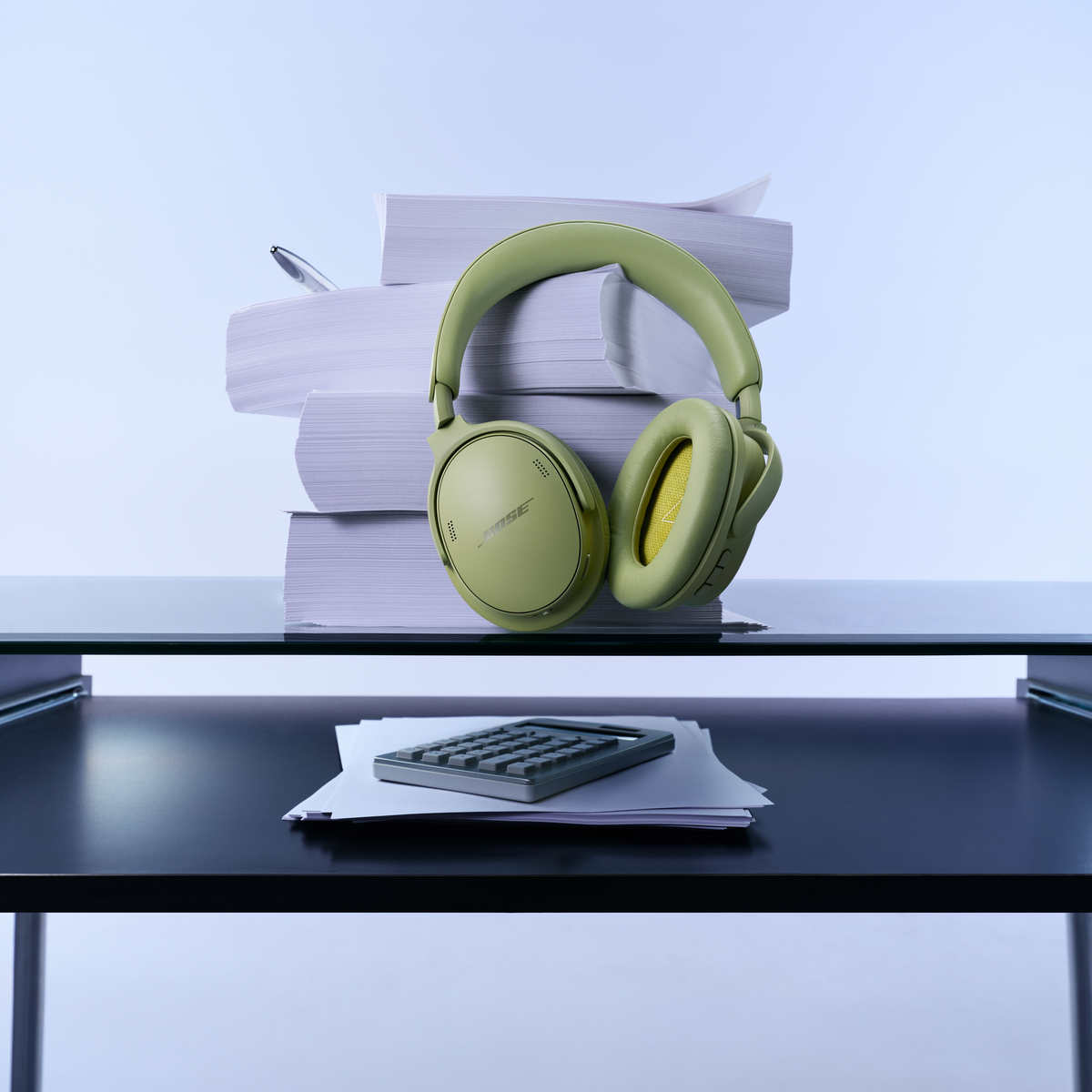 Casque vert devant une pile de papier sur une étagère en verre, avec une calculatrice en bas.