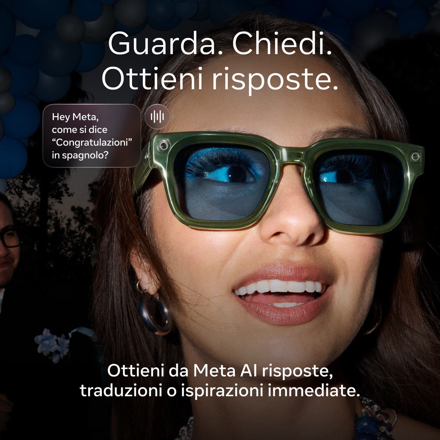 Una donna con occhiali smart dalla montatura verde e lenti blu sorride all'aperto con palloncini blu sullo sfondo.