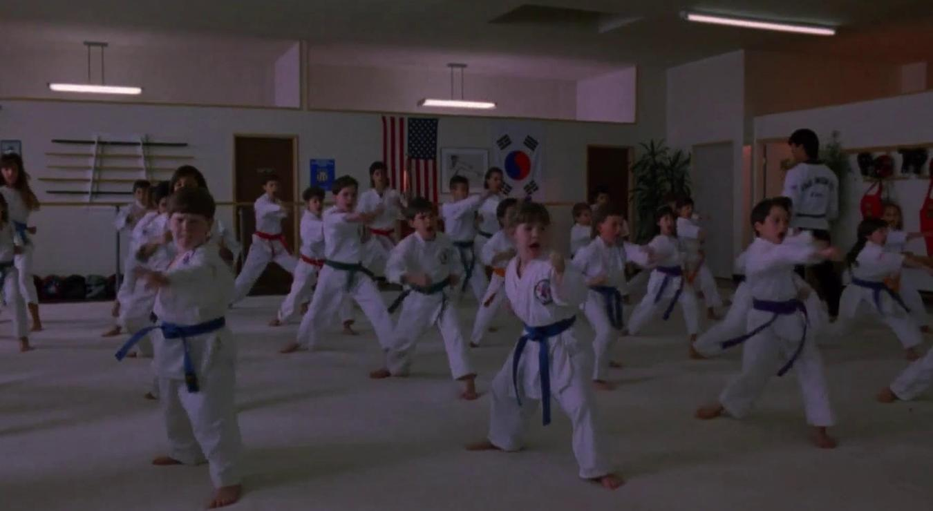 Kinder in weißen Karate-Anzügen mit farbigen Gürteln üben Kampfkunst-Posen in einem beleuchteten Dojo.