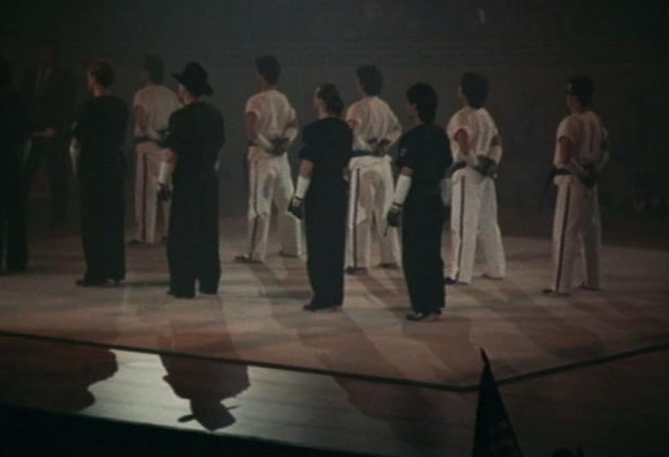 Martial-Arts-Schüler in Schwarz-Weiß-Uniformen stehen in einer Sporthalle und blicken nach vorn.
