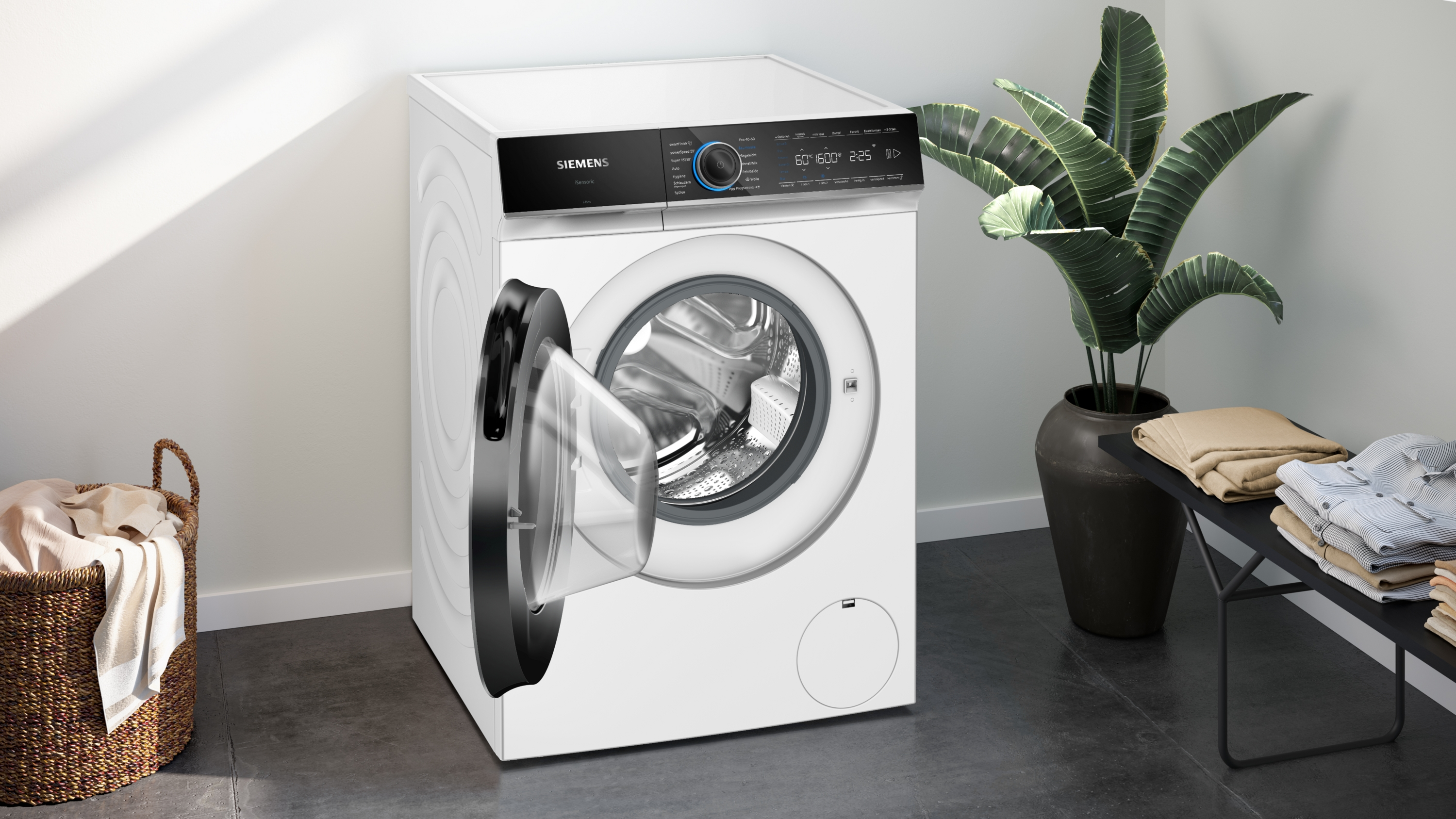 Eine weiße Siemens-Waschmaschine mit offener Tür steht in einem modernen Raum mit einer Pflanze und Kleidung.