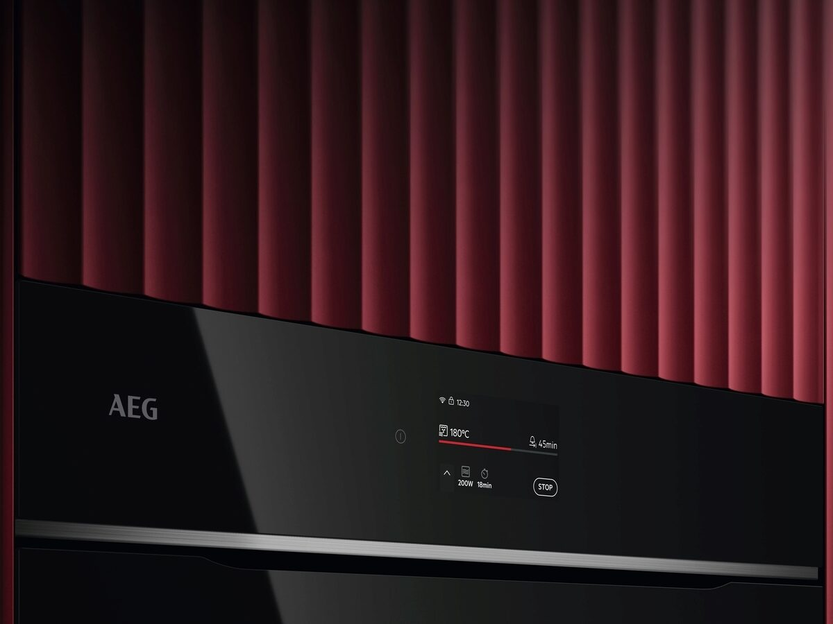 Un horno AEG con panel de control negro y pantalla digital sobre fondo estriado rojo.