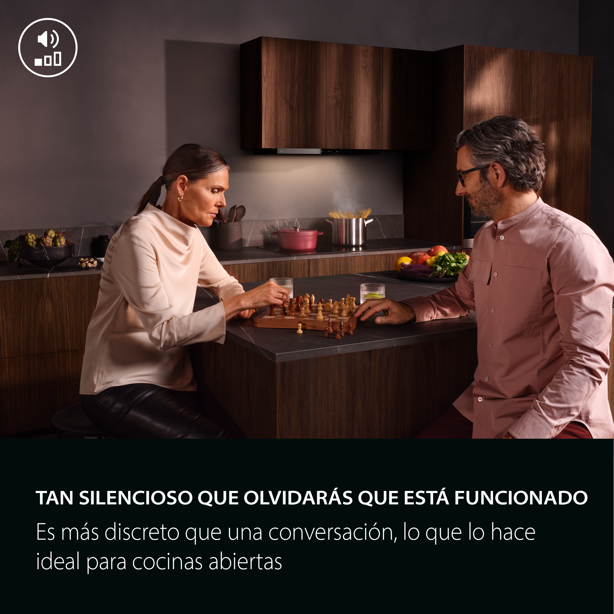Una pareja juega al ajedrez en una isla de cocina oscura ante armarios de madera.