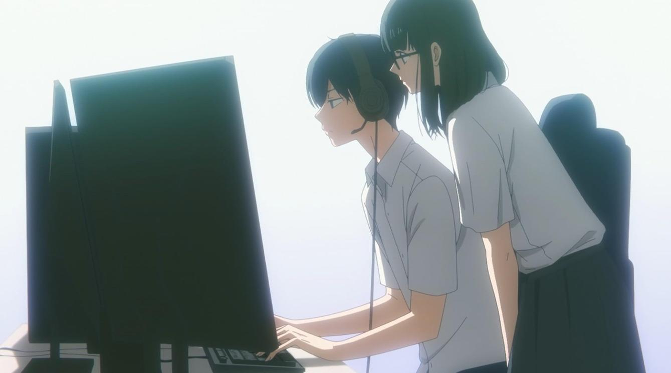 Ein Junge mit Headset sitzt vor einem Computer, während ein Mädchen mit Brille hinter ihm steht und zuschaut.