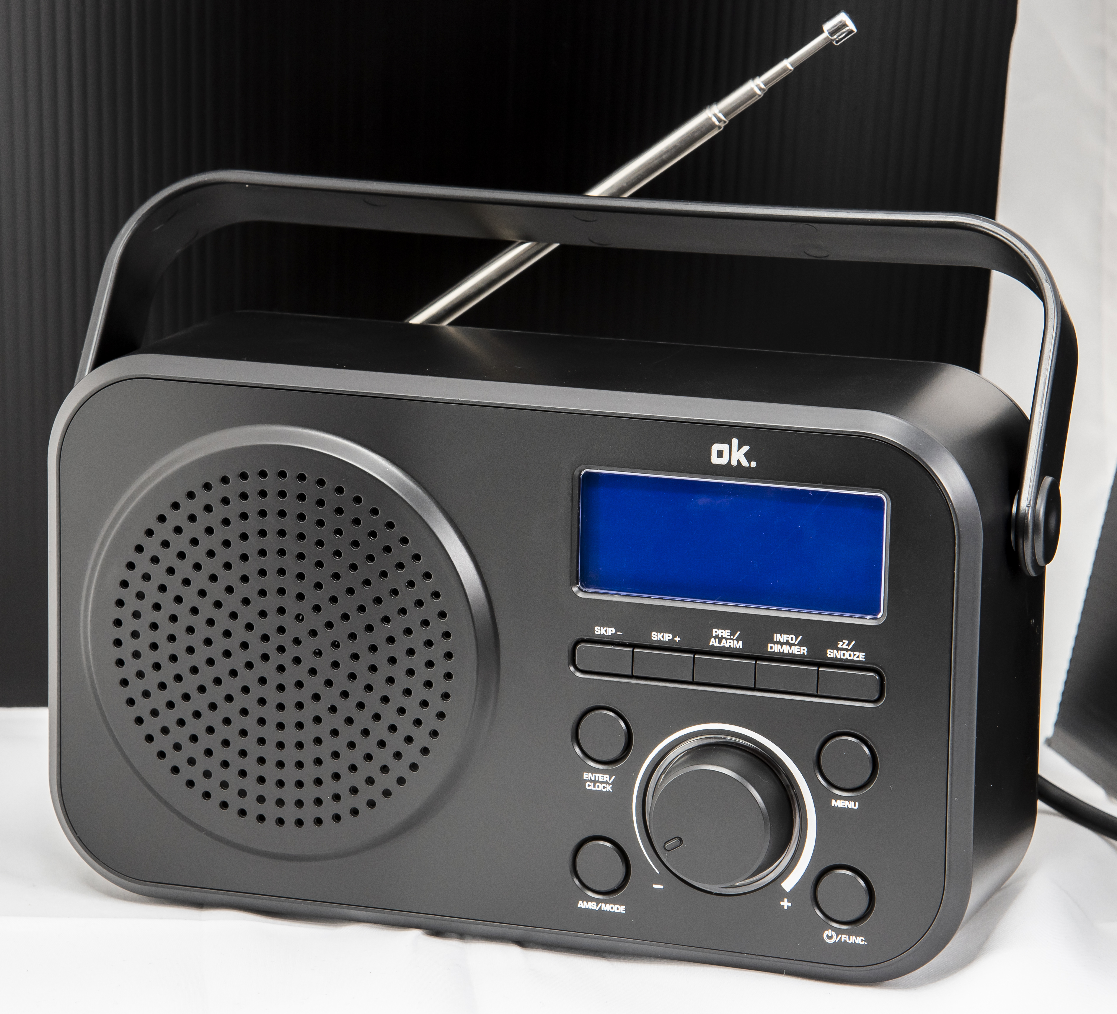 Ein schwarzes ok. Radio mit ausziehbarer Antenne, Lautsprecher und blauer LCD-Anzeige vor dunklem Hintergrund.