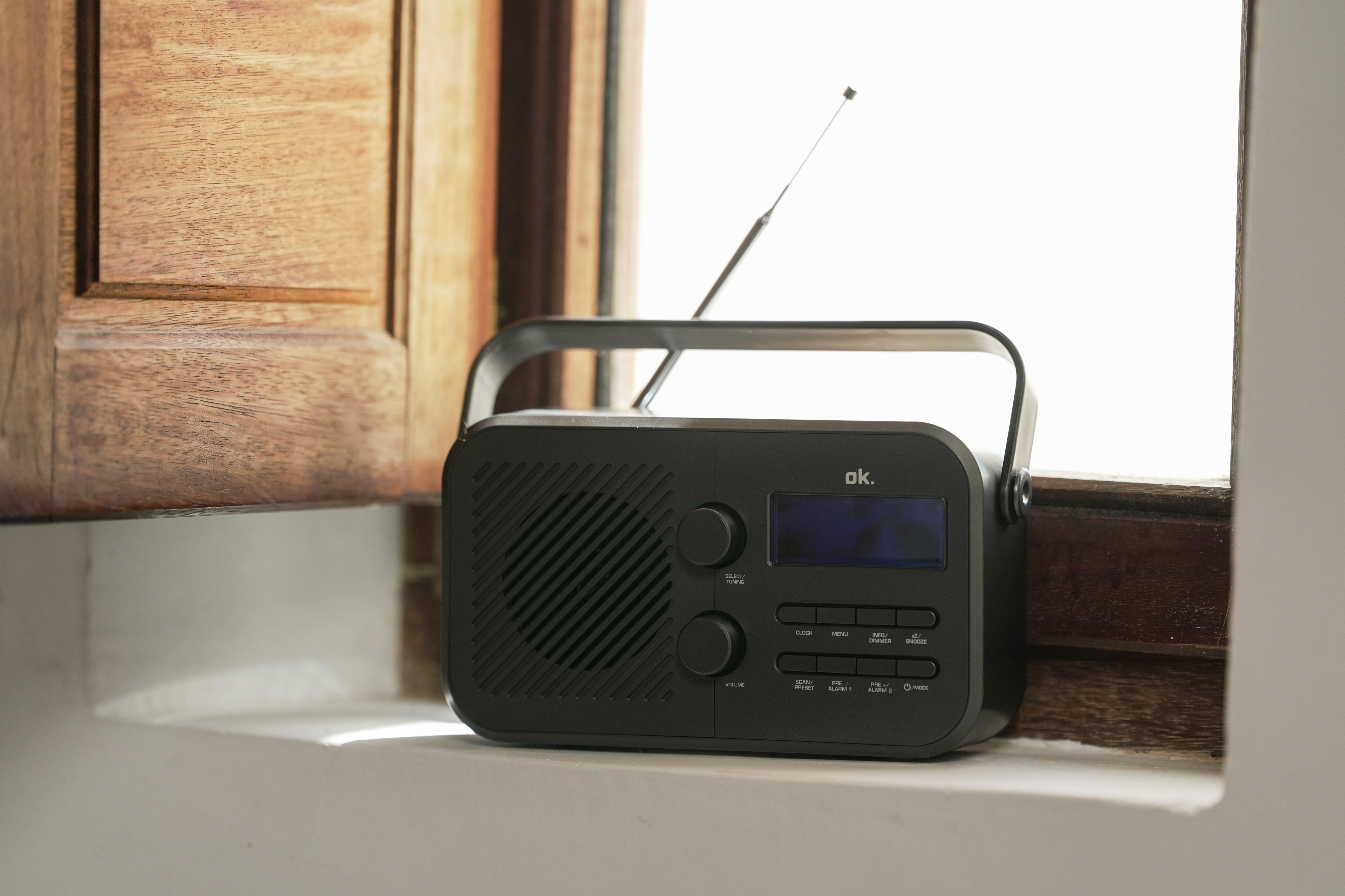 Ein schwarzes Radio mit ausgefahrener Antenne steht auf einer Fensterbank vor einem Holzfenster.