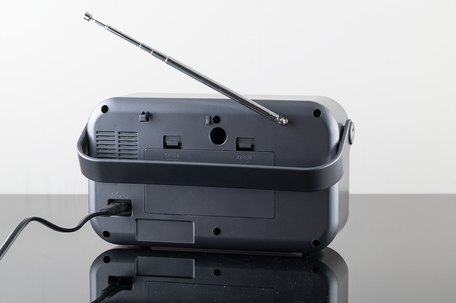 Rückseite eines grauen Radios mit ausgefahrener Teleskopantenne und angeschlossenem Netzkabel auf einem Tisch.
