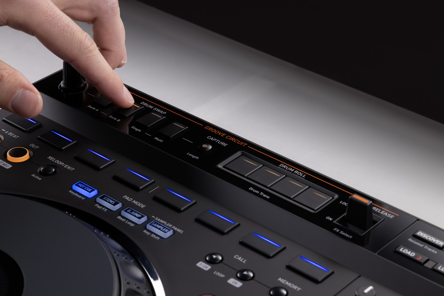 Una mano ajusta botones y controles en un controlador de DJ negro con luces azules y naranjas.