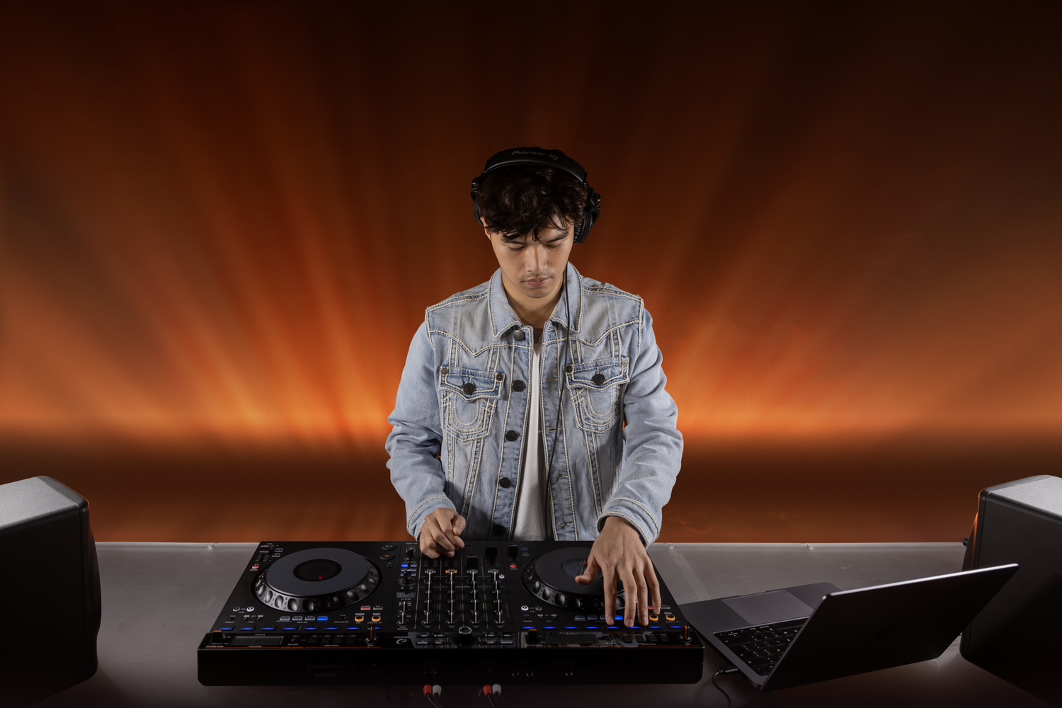 DJ con chaqueta de mezclilla mezcla música bajo luz cálida.