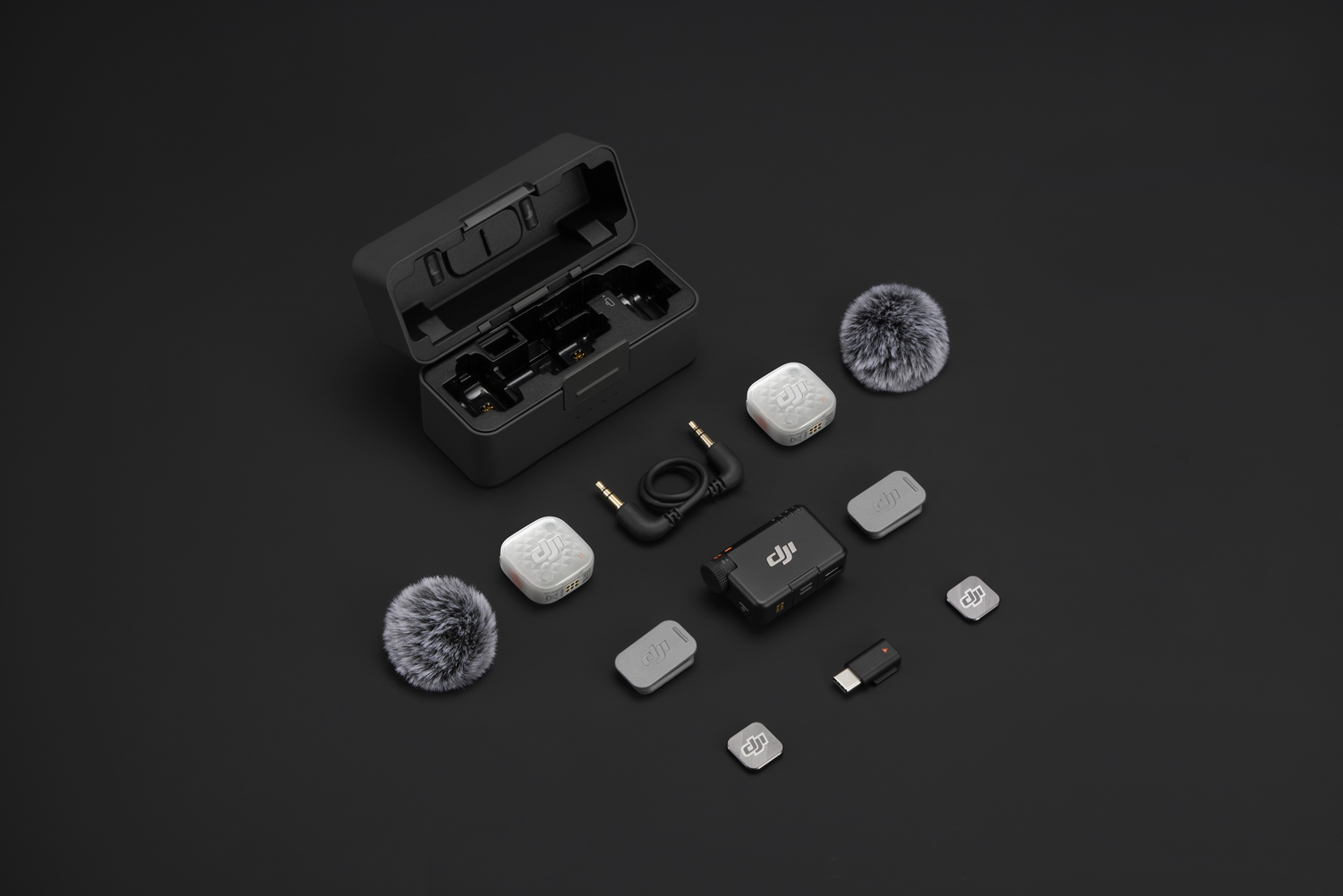 Sistema de micrófono DJI con estuche de carga, transmisores, receptor, antivientos y adaptadores en fondo negro.