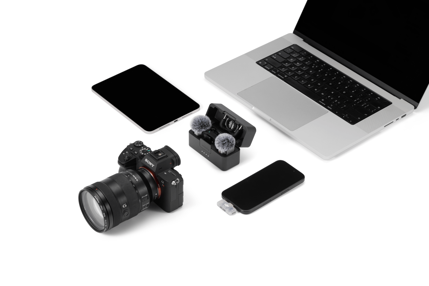 Portátil, tableta, cámara Sony, micrófonos inalámbricos y smartphone sobre fondo blanco.