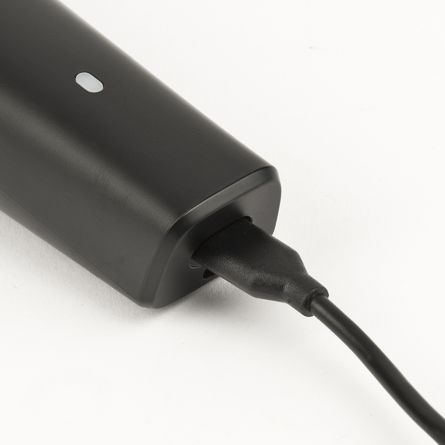 Un dispositivo elettronico nero è in carica con un cavo nero su una superficie bianca.