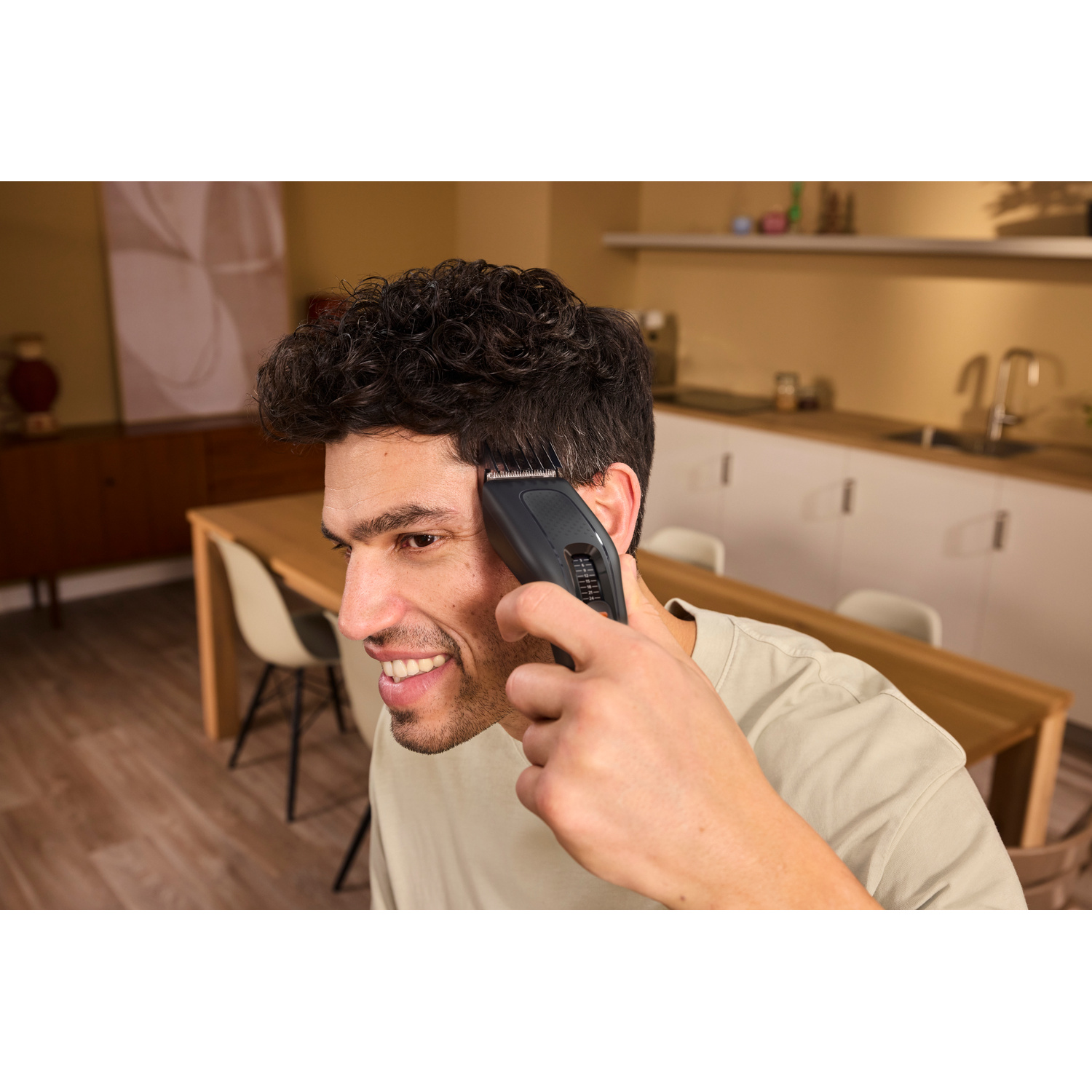 Un uomo sorridente si taglia i capelli ricci con un tagliacapelli in cucina.