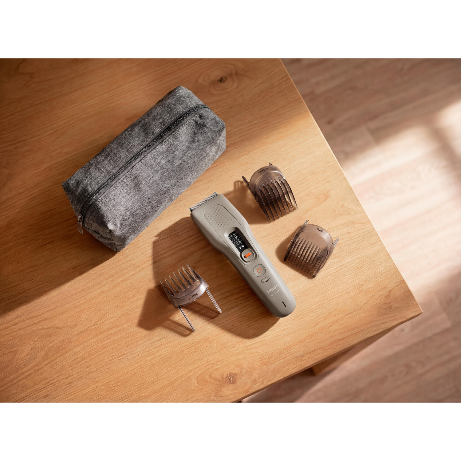 Un tagliacapelli grigio, tre accessori e una custodia grigia disposti su un tavolo di legno.