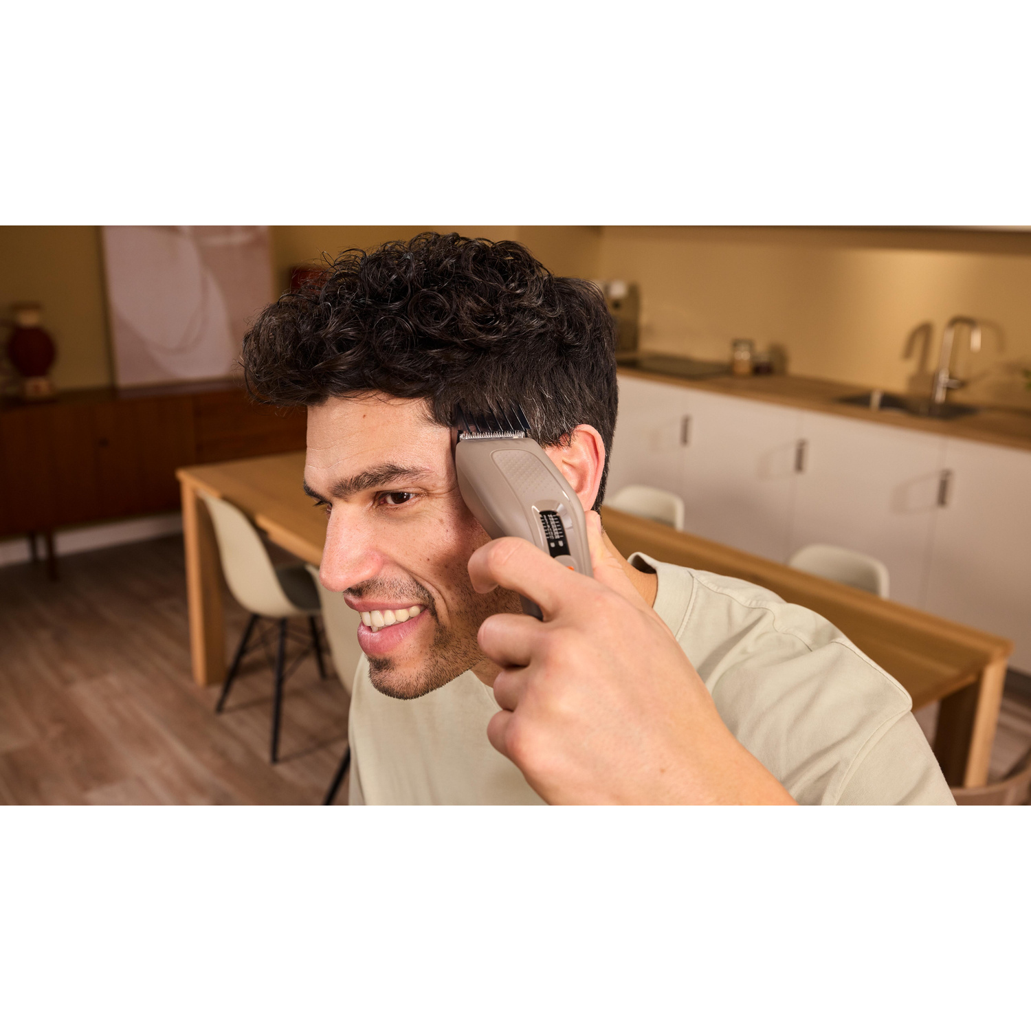 Un uomo si taglia i capelli con un tagliacapelli grigio a casa in cucina.