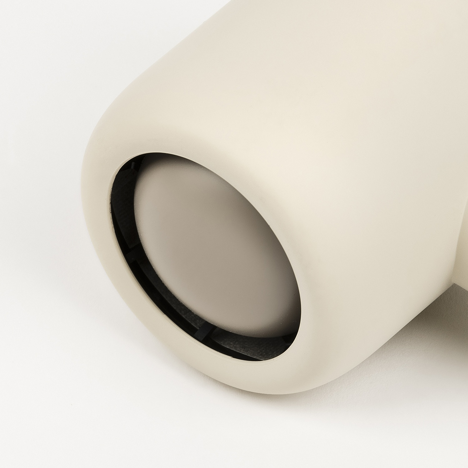 Un apparecchio di illuminazione cilindrico color crema con inserto rotondo su sfondo bianco.