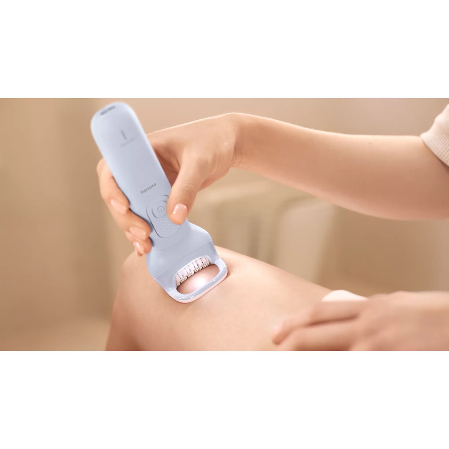 Una persona usa un epilatore Philips azzurro sulla gamba davanti a uno sfondo sfocato.