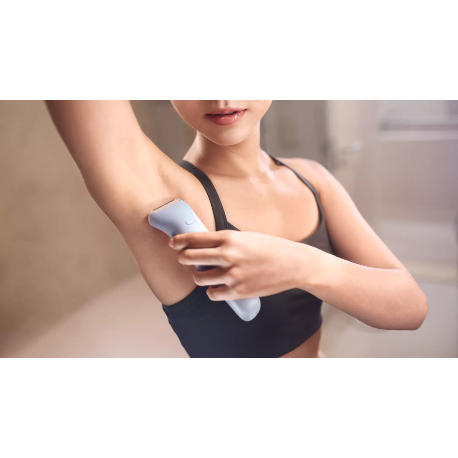 Una donna con top sportivo nero si rade l'ascella con un rasoio blu.