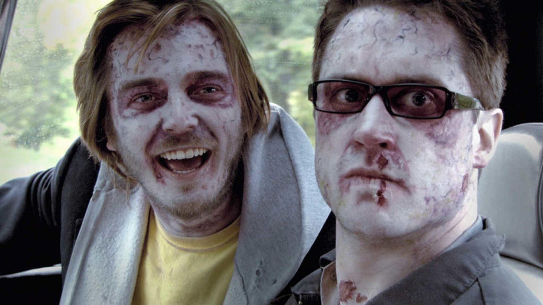 Zwei junge Männer mit Zombie-Make-up, blassem Gesicht und Wunden schauen in die Kamera.
