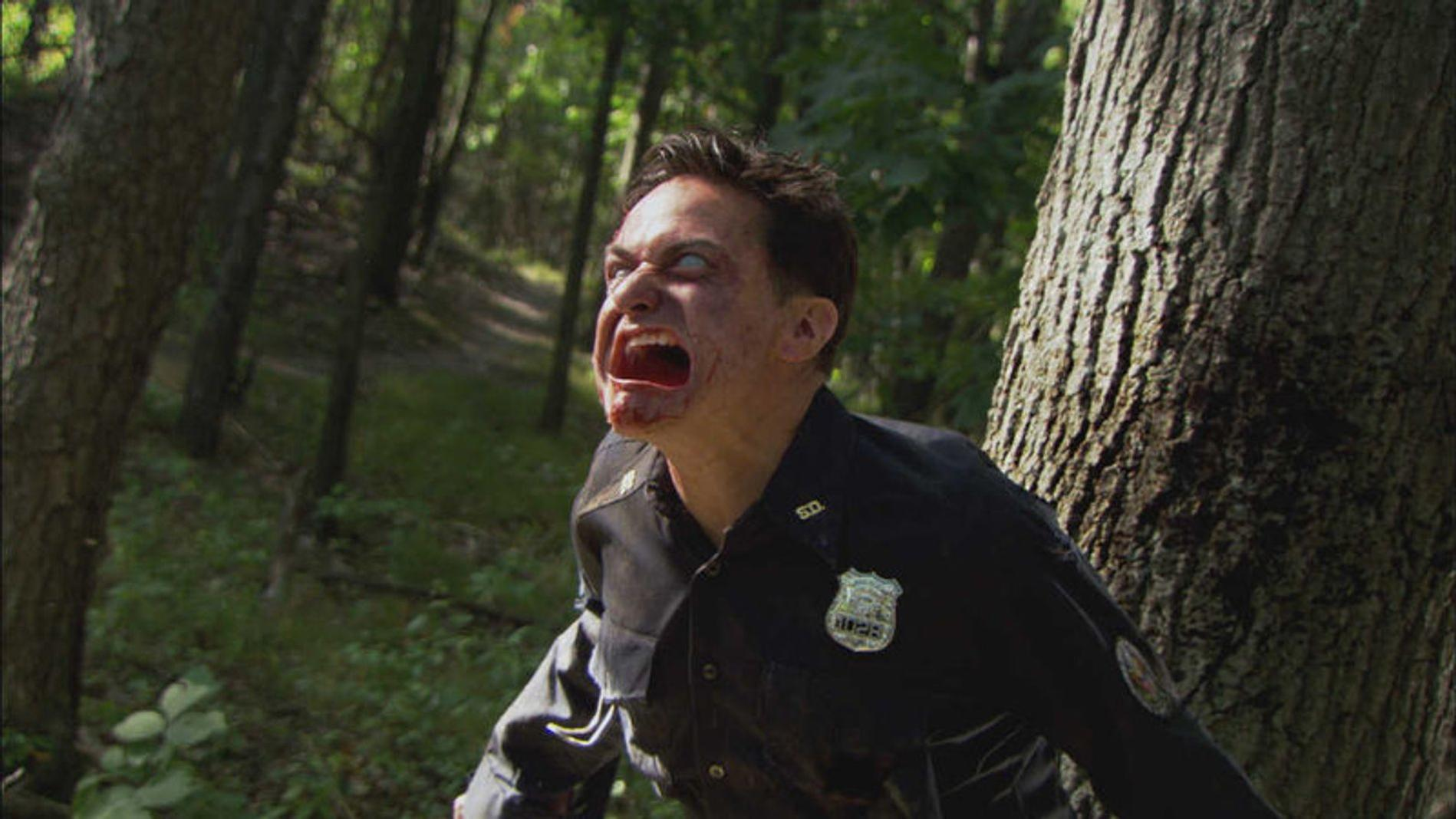 Ein Mann im Polizeikostüm schreit mit blutverschmiertem Mund im Wald.