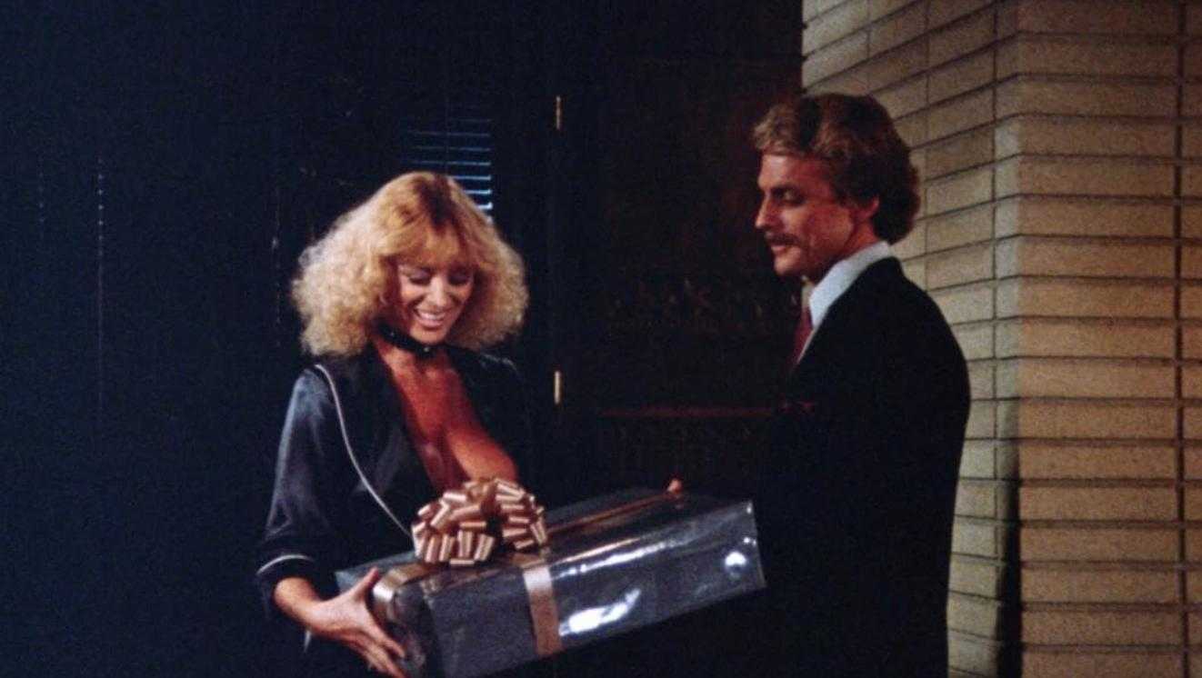 Ein blondes Mädchen und ein Mann halten ein großes Geschenk vor einer Backsteinwand.