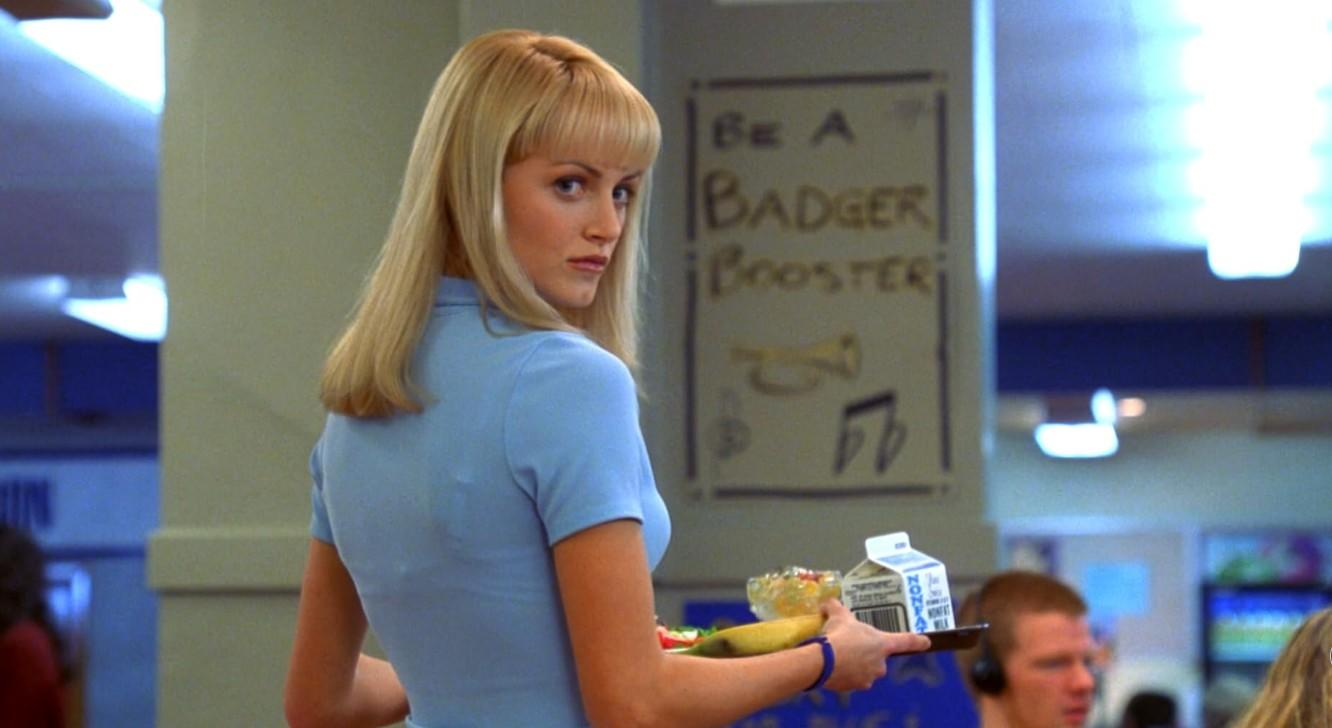 Eine blonde Frau hält in einer Kantine ein Tablett mit Essen.