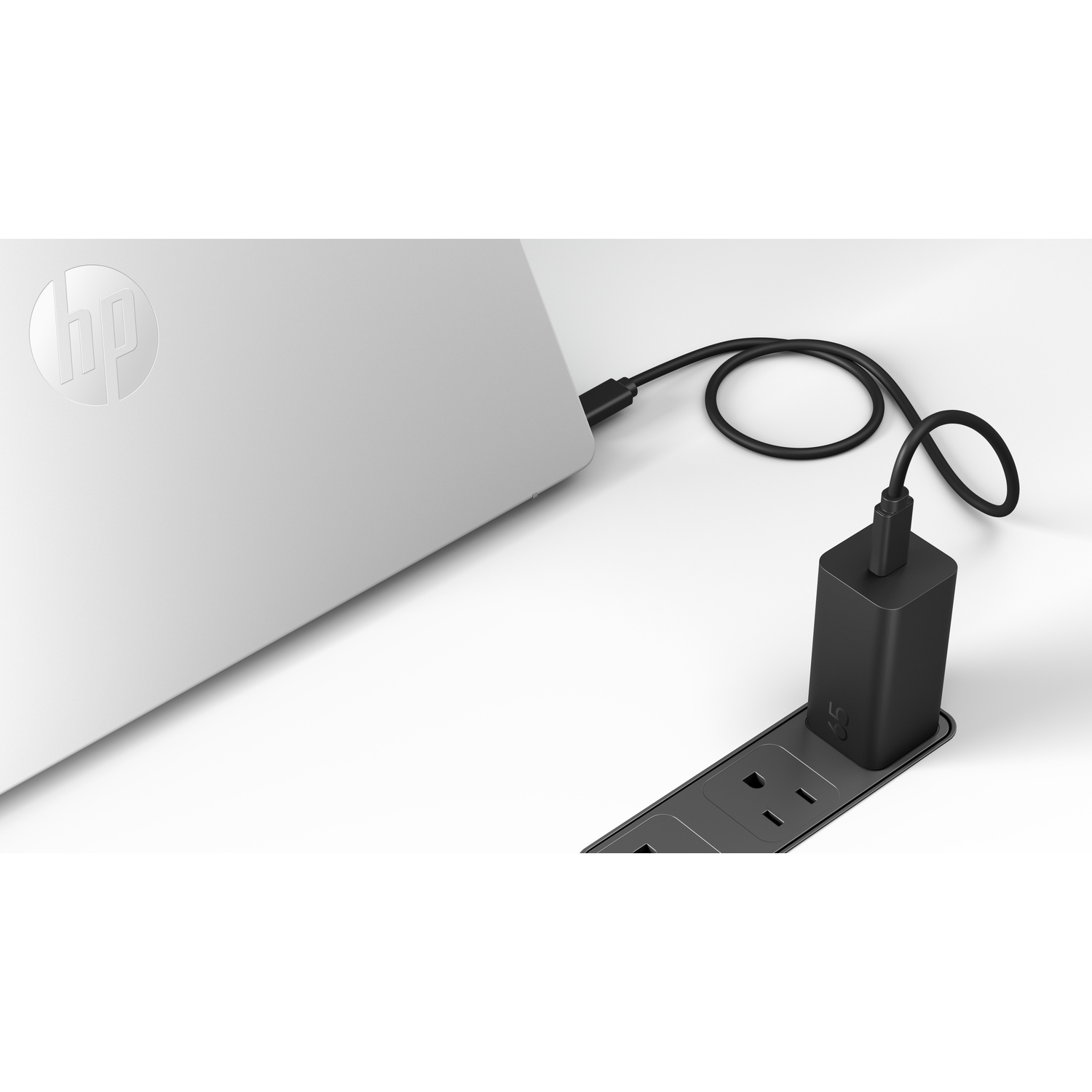 A silver HP laptop connected to a black wall charger plugged into a power strip on a white surface.
