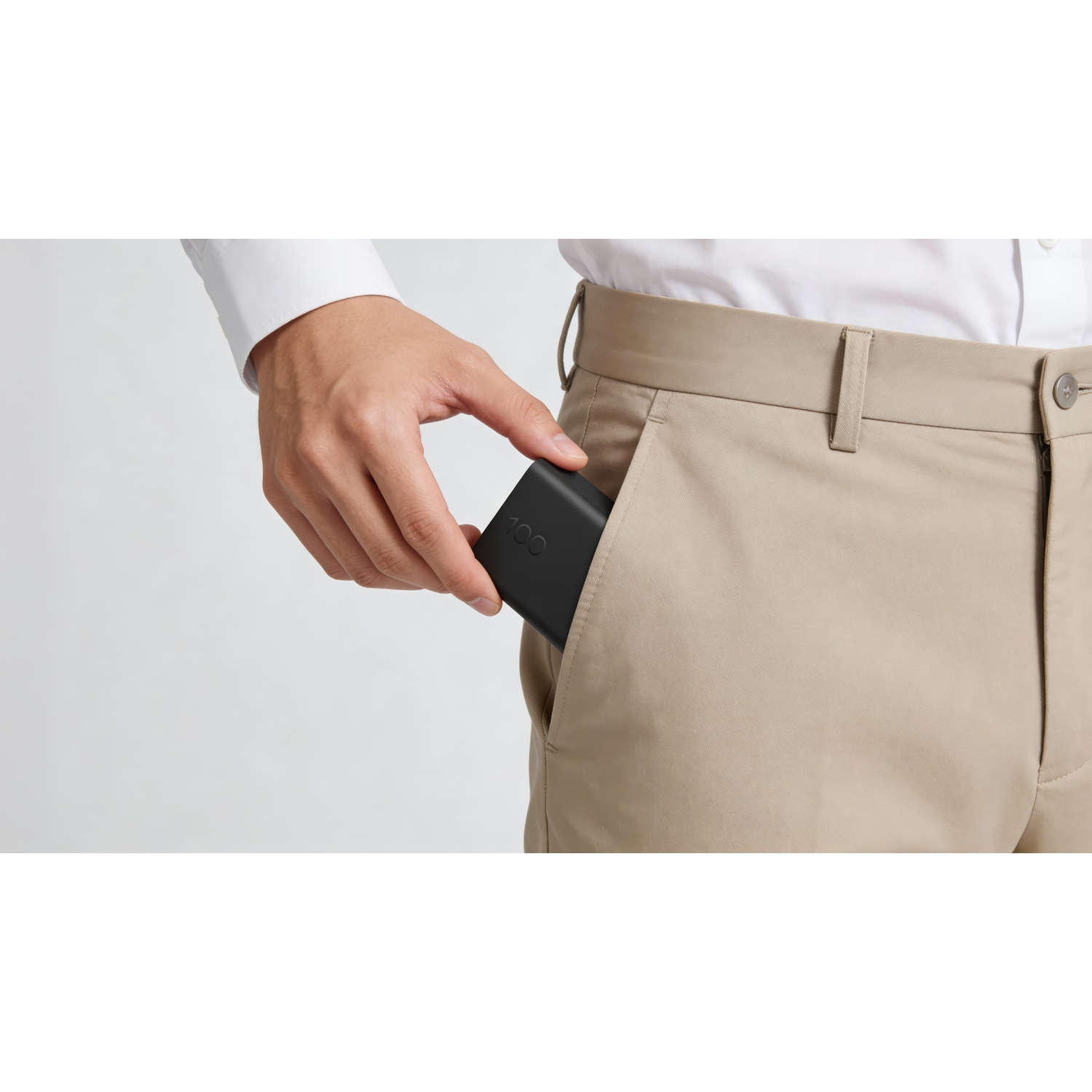 A person in a white shirt and khaki pants places a black rectangular device into their front pocket.