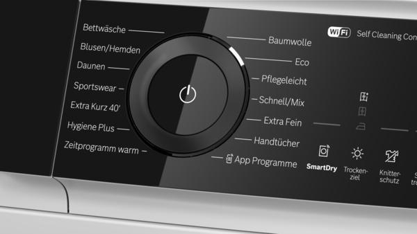 Bedienfeld einer Waschmaschine mit Drehregler, Ein-Aus-Symbol und deutschen Programmbeschriftungen.