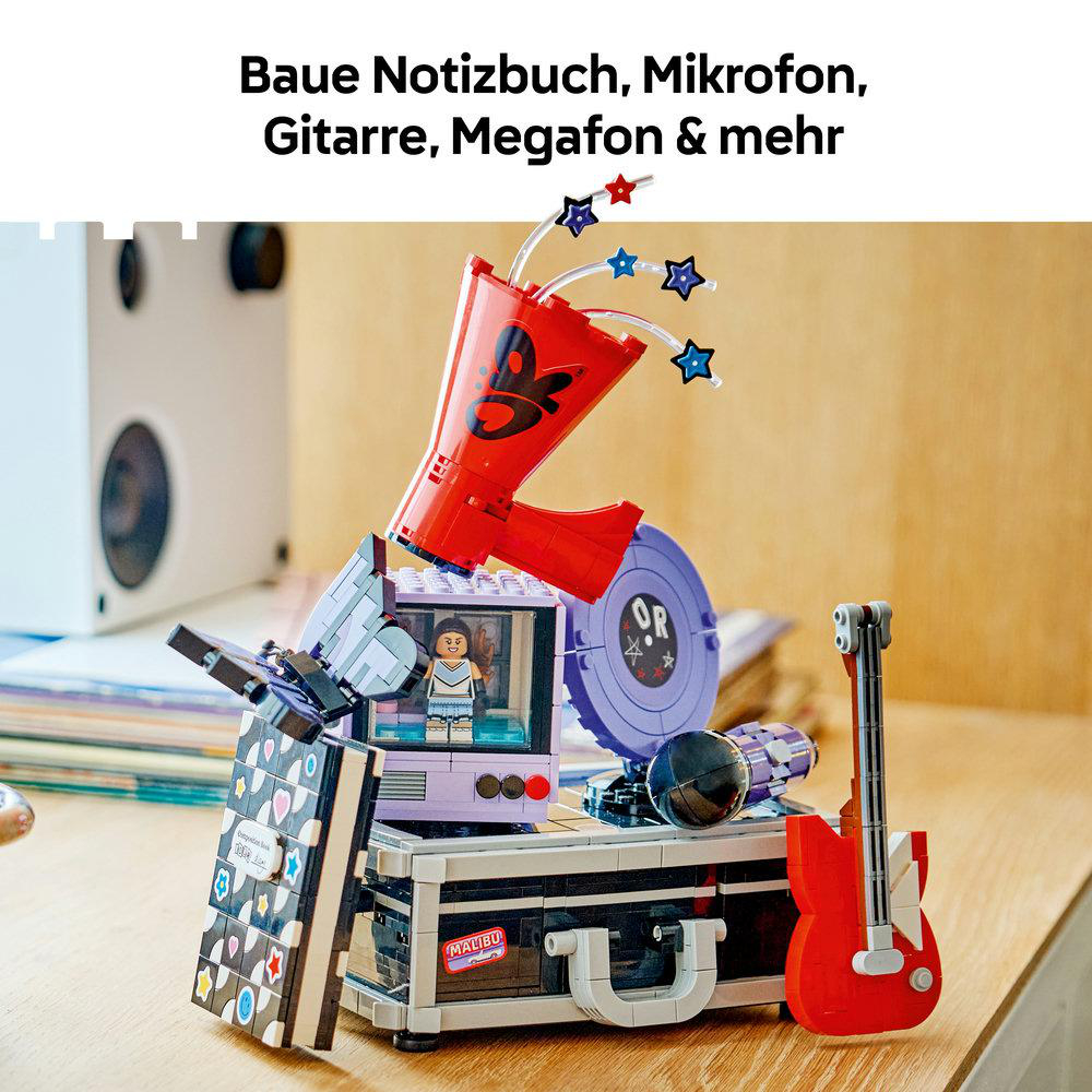 Lego-Modell einer Bühne mit Megafon, Gitarre, Mikrofon und Notizbuch auf Holztisch.