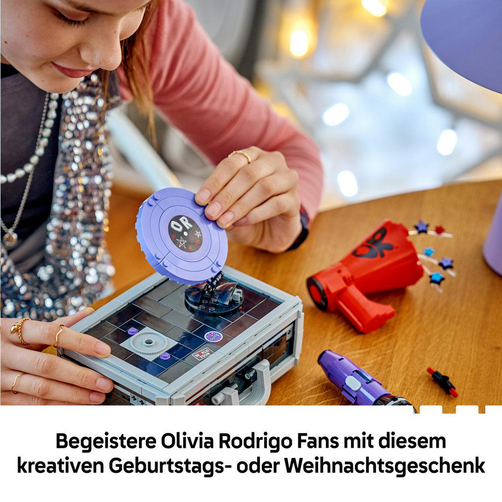 Ein Kind baut ein Lego Set mit Musik- und Olivia Rodrigo-Themen auf einem Holztisch zusammen.