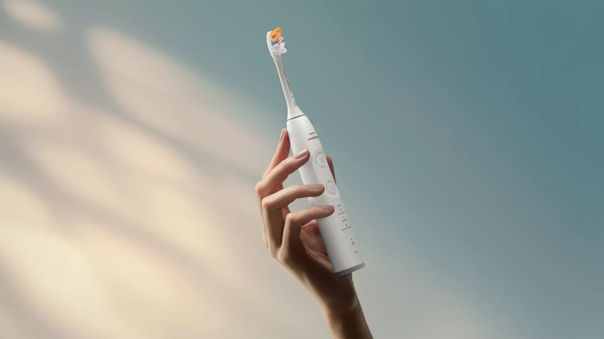 Eine Hand hält eine weiße elektrische Zahnbürste vor einem blauen Hintergrund mit Lichteffekten.