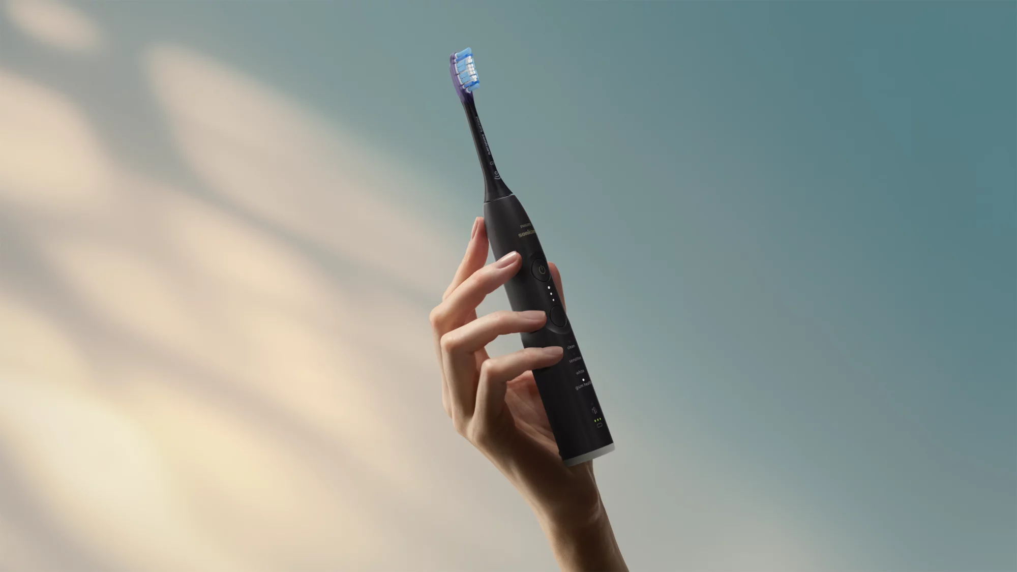 Eine Hand hält eine schwarze elektrische Zahnbürste vor einem blau-grauen, beleuchteten Hintergrund.