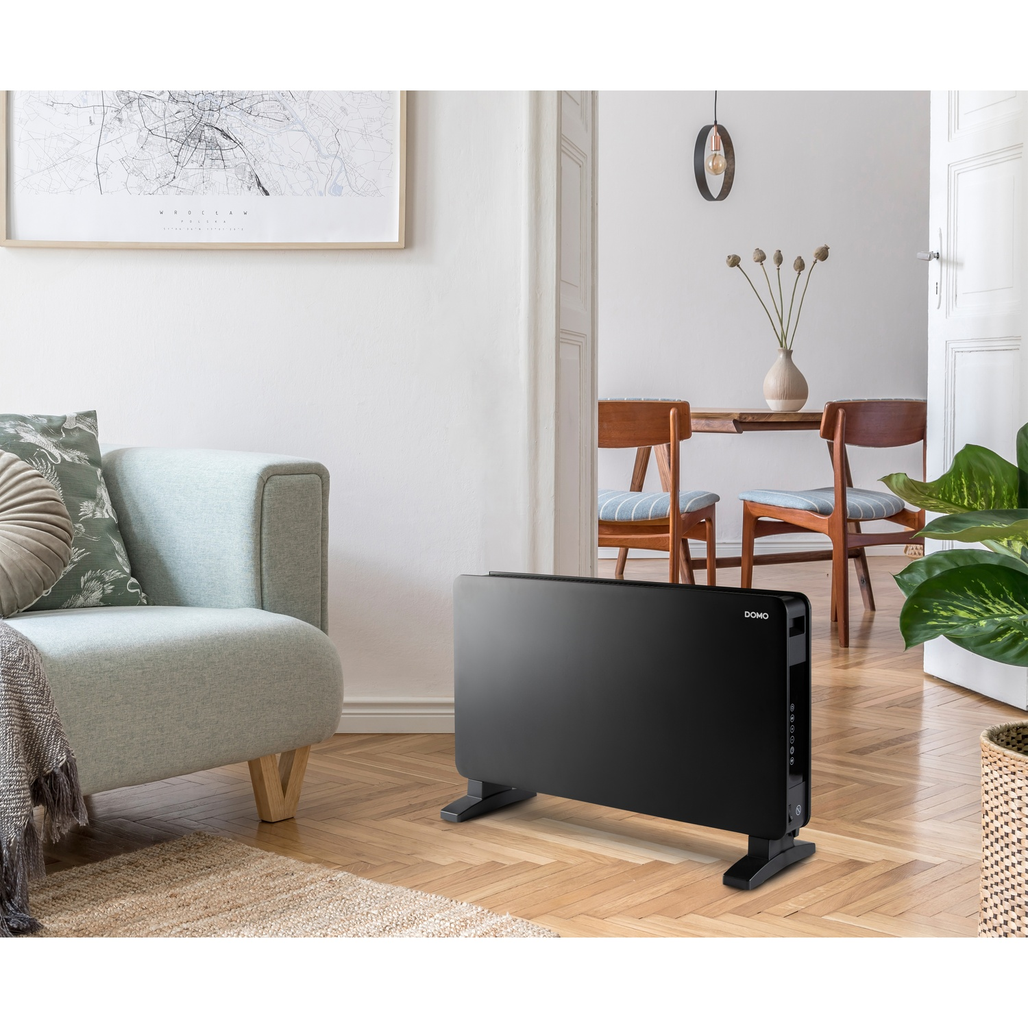 A black convector heater stands on a wooden floor in a bright living room.