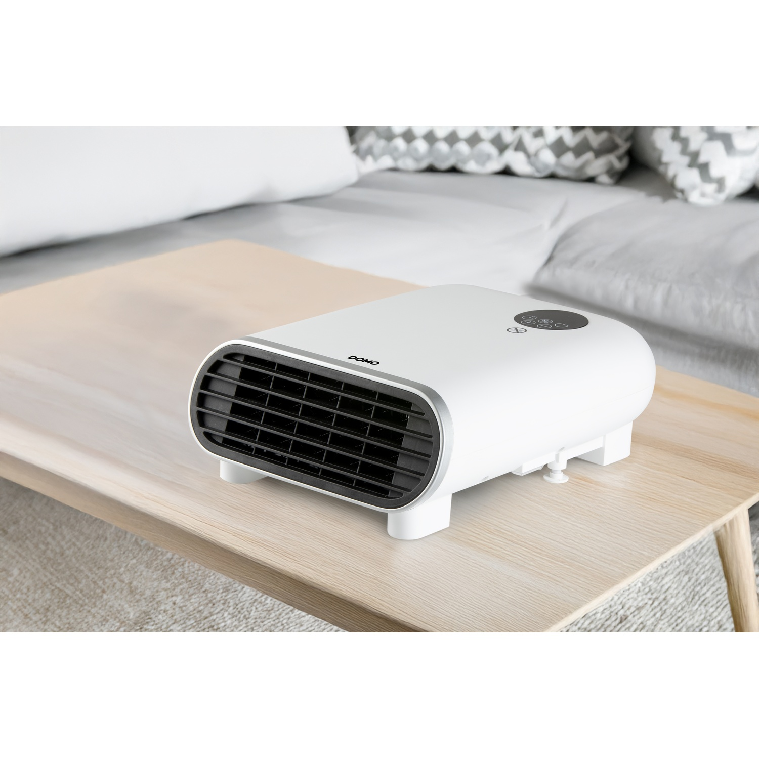 A white fan heater with a black grille stands on a wooden table in front of a sofa.