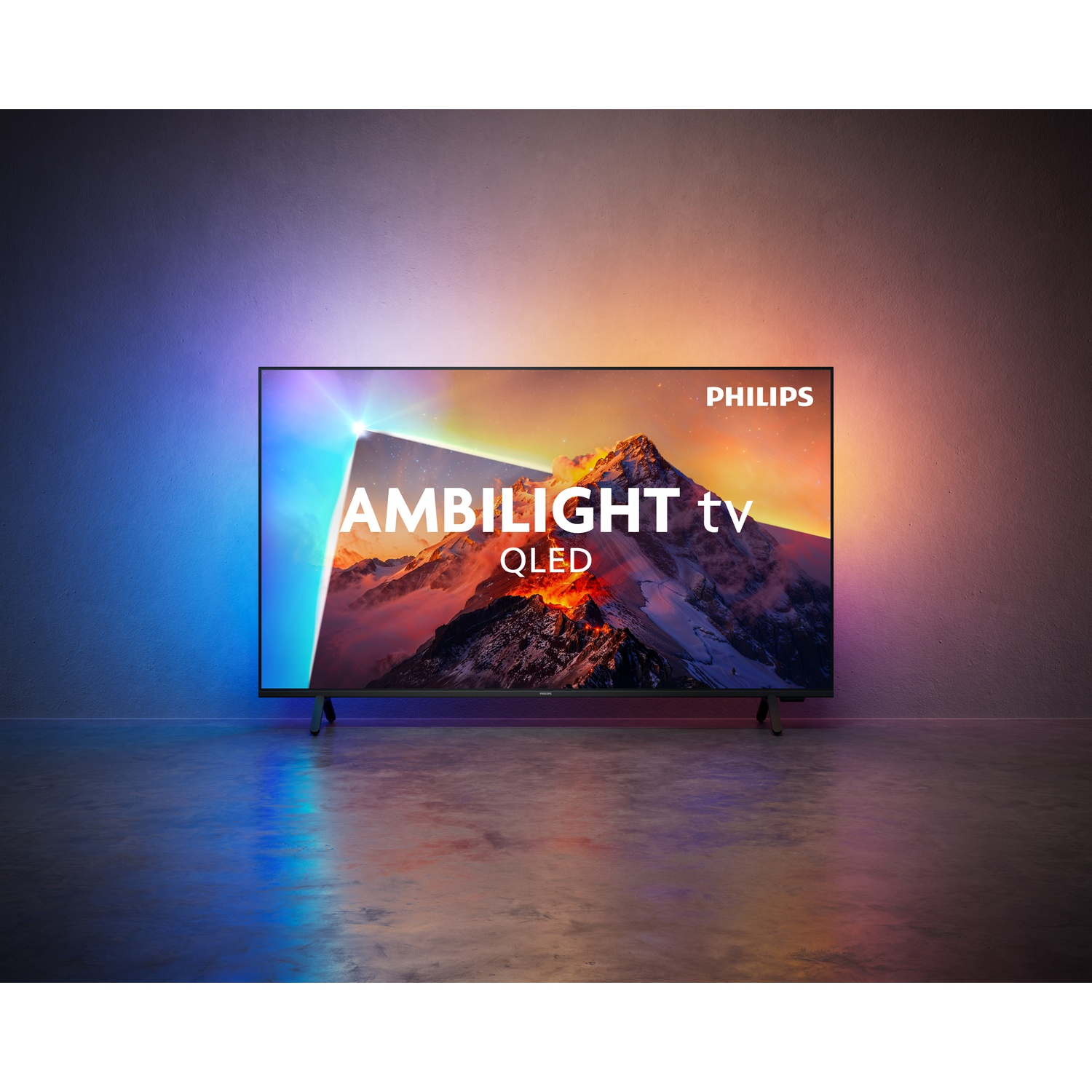 A Philips Ambilight QLED TV on the floor, casting colorful light onto the wall.