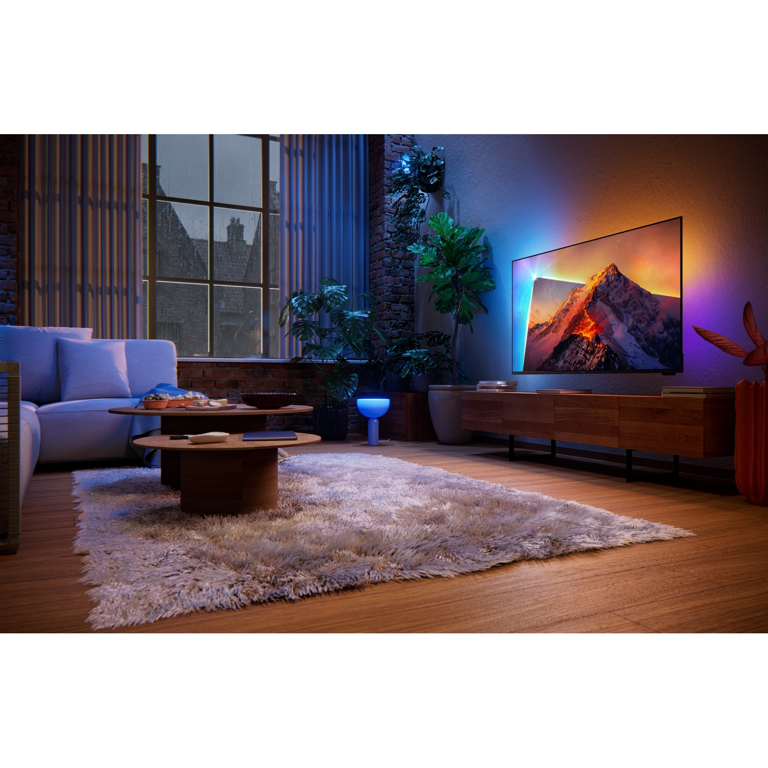 Living room with sofa, wooden tables, large screen displaying a mountain, and plants.