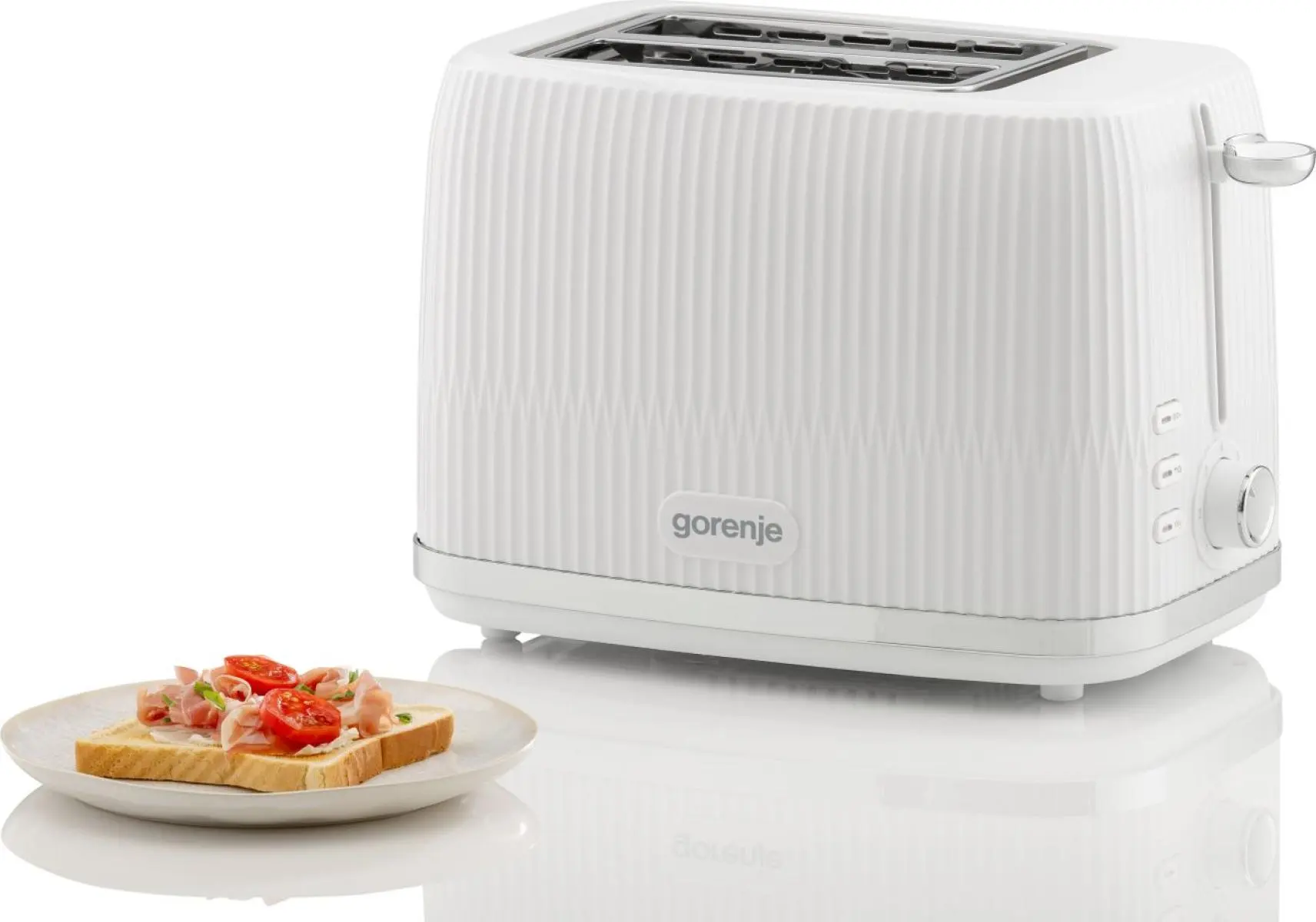 Egy fehér Gorenje kenyérpirító fehér felületen, egy tányér pirítós, sonka és paradicsom mellett.