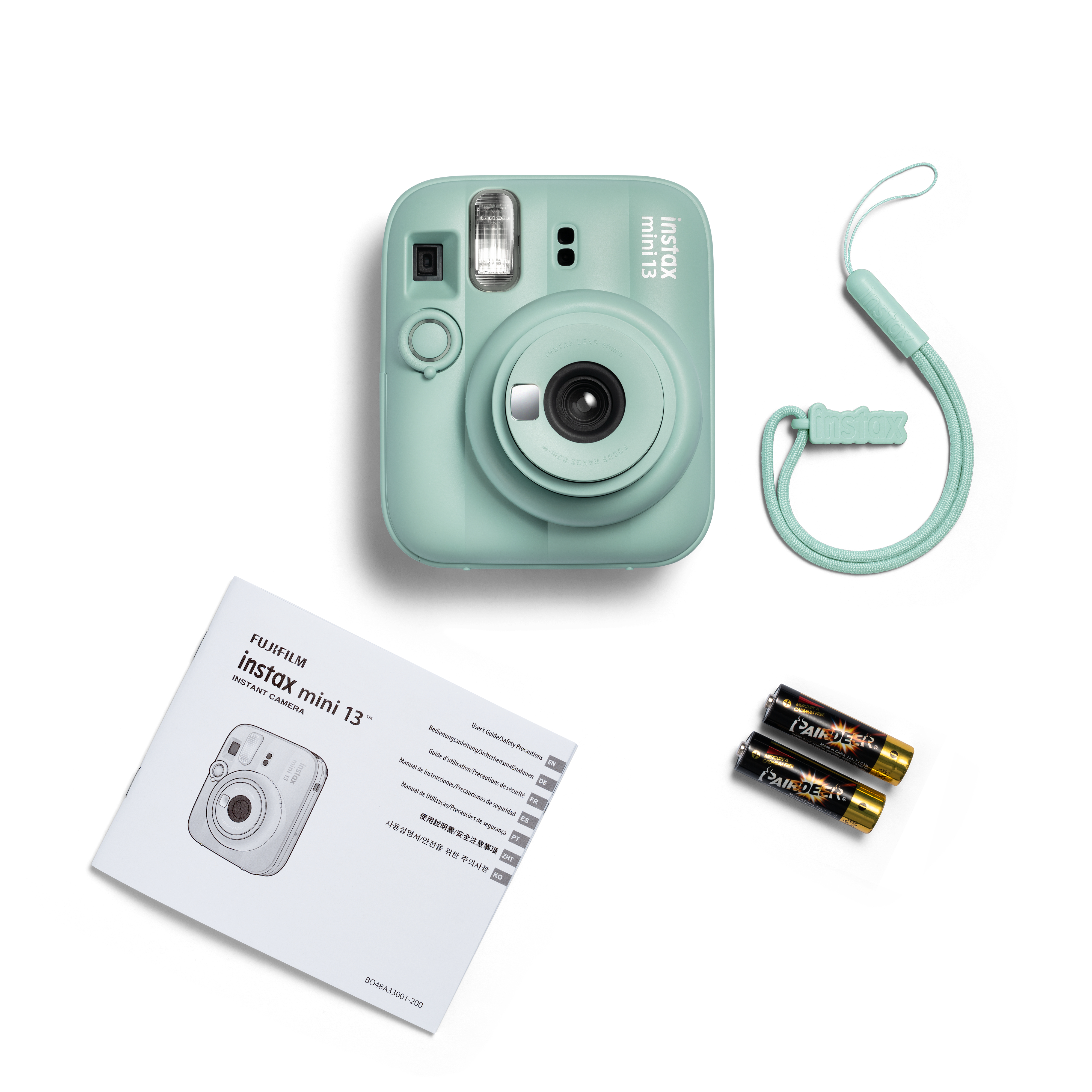 Pastellgrüne Instax Mini 13 Sofortbildkamera mit Bedienungsanleitung, Handschlaufe und zwei Batterien auf weißem Grund.